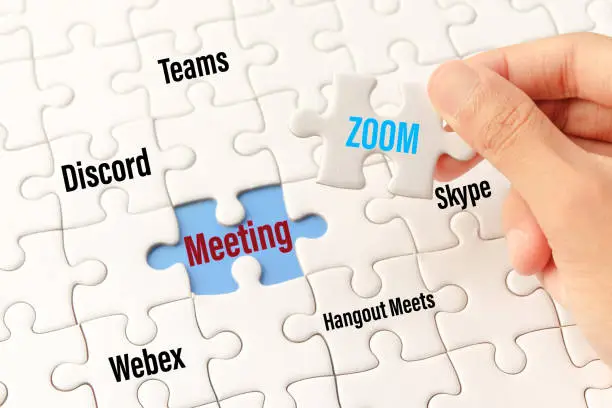 Bangkok, Thailand - May 10, 2020 : Hand holding zoom word on white jigsaw puzzle is connect to meeting word on blue gap - idea match (Teams, Discord, webex, Hangout Meets, skype) concept.Bangkok, Thailand - May 10, 2020 : Hand holding zoom word on white jigsaw puzzle is connect to meeting word on blue gap - idea match (Teams, Discord, webex, Hangout Meets, skype) concept.