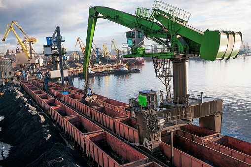 Balanced Hydraulic Crane - The manipulator unloads bulk cargo from industrial wagons in the seaport.