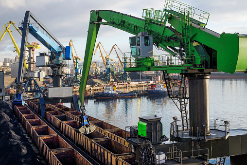 Balanced Hydraulic Crane - The manipulator unloads bulk cargo from industrial wagons in the seaport.