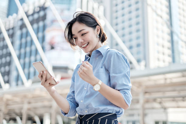 una hermosa mujer de negocios asiática está mirando su teléfono inteligente y muy feliz. - asia fotografías e imágenes de stock
