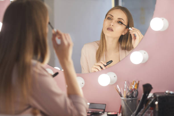 istock Beautiful Young Woman Looking in Mirror and Applying Make up 1224014580