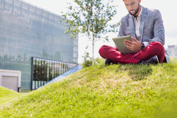 istock Portrait of young attractive businessman using digital tablet while sitting on the grass 1224018126