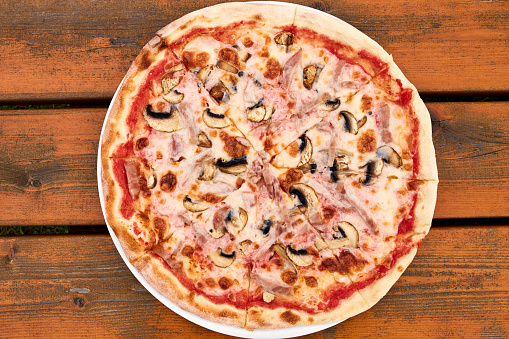 A ham and mushroom pizza sitting on top of a wooden tableundefined