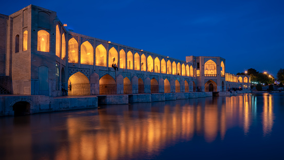 Isfahan, Iran - May 2019: Khaju bridge over Zayandeh river at dusk with lights during blue hour