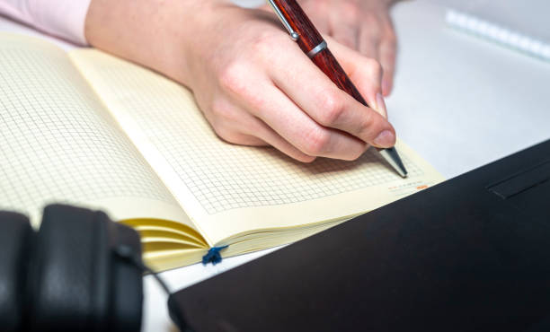 istock Female hands is writing smth on notebook with laptop notebook pen around on white table. Online business 1224022410