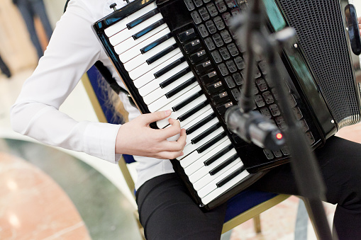The musician plays the accordion sitting on a chair in front of the microphone. The concept of performing and recording the melody