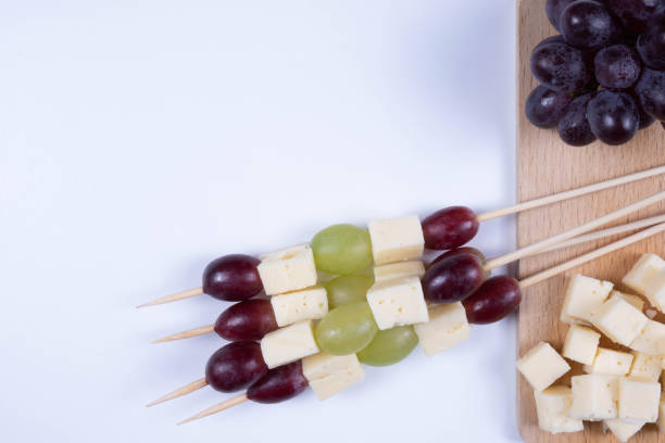 slices of cheese and grapes put on shpis on a table on a white background