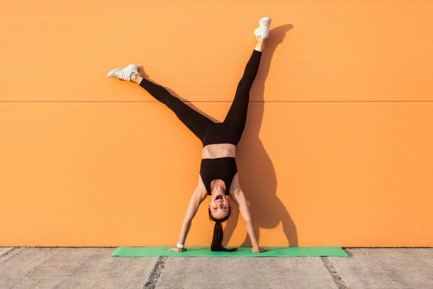 Overjoyed excited girl with perfect athletic body in tight sportswear doing yoga handstand pose against wall and laughing Overjoyed excited girl with perfect athletic body in tight sportswear doing yoga handstand pose against wall and laughing, shouting from happiness. Gymnastics for body balance outdoor workouts yoga pants photos stock pictures, royalty-free photos & images