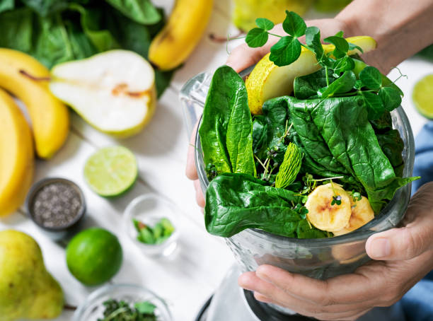 Woman is preparing a healthy detox drink in a blender - a smoothie with fresh fruits, green spinach and superfood seeds. Healthy lifestyle concept, ingredients for smoothies on the table, top view stock photo