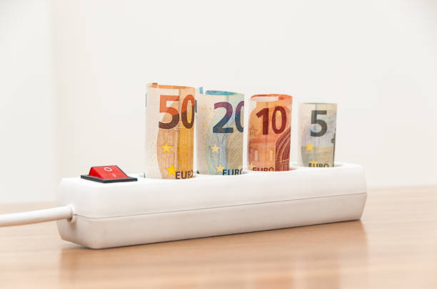 Euro banknotes inserted into an extension socket on a wooden surface. Expensive concepts of energy and cost of electricity. Front view.