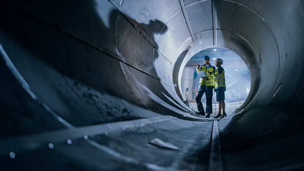 istock Two Heavy Industry Engineers Walking Inside Pipe, Use Laptop, Have Discussion, Checking Design. Construction of the Oil, Natural Gas and Biofuels Transport Pipeline. Industrial Manufacturing Factory 1224034031
