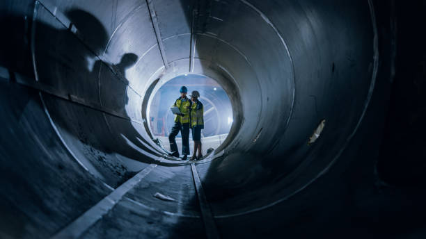 istock Two Heavy Industry Engineers Walking Inside Pipe, Use Laptop, Have Discussion, Checking Design. Construction of the Oil, Natural Gas and fuels Transport Pipeline. Industrial Manufacturing Factory 1224034040