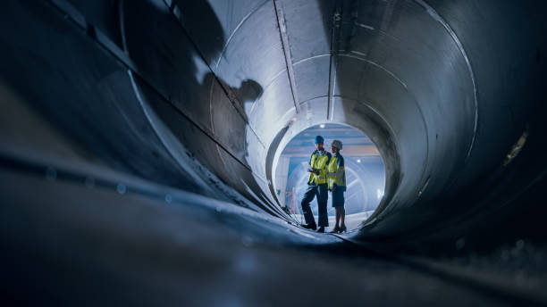 istock Two Heavy Industry Engineers Walking Inside Pipe, Use Laptop, Have Discussion, Checking Design. Construction of the Oil, Natural Gas and Biofuels Transport Pipeline. Industrial Manufacturing Factory 1224034049