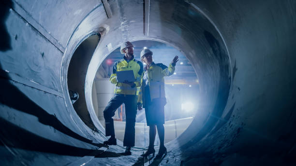 istock Two Heavy Industry Engineers Walking Inside Pipe, Use Laptop, Have Discussion, Checking Design. Construction of the Oil, Natural Gas and Biofuels Transport Pipeline. Industrial Manufacturing Factory 1224034059