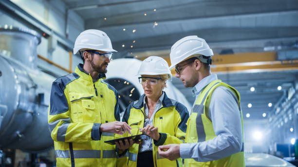 Three Heavy Industry Engineers Stand in Pipe Manufacturing Factory, Use Digital Tablet Computer, Have Discussion. Large Pipe Assembly. Design and Construction of Oil, Gas and Fuels Transport Pipeline Three Heavy Industry Engineers Stand in Pipe Manufacturing Factory, Use Digital Tablet Computer, Have Discussion. Large Pipe Assembly. Design and Construction of Oil, Gas and Fuels Transport Pipeline hard hat stock pictures, royalty-free photos & images