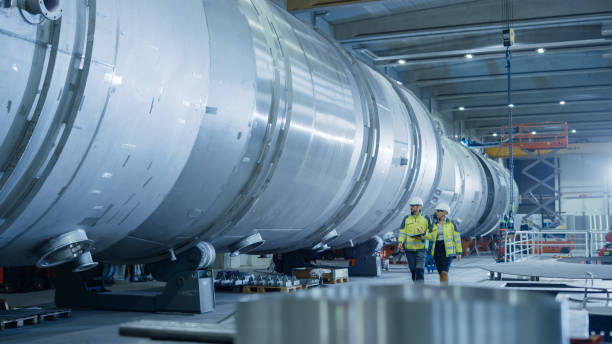 istock Two Heavy Industry Engineers Walking Through Pipe Manufacturing Facility, Use Digital Tablet, Have Discussion. Modern Industrial Design and Construction of Oil, Gas and Fuels Transport Pipeline 1224034102