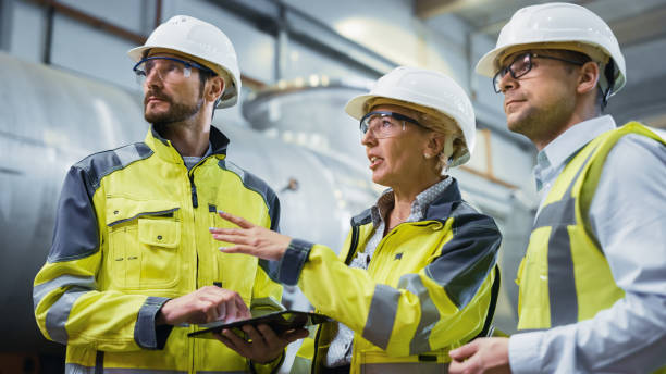 trois ingénieurs de l’industrie lourde se tiennent dans l’usine de fabrication de tuyaux, utilisent l’ordinateur numérique de tablette, ont la discussion. grand tuyau assemblé. conception et construction d’un pipeline de transport de pétrole, d - tenue de protection photos et images de collection