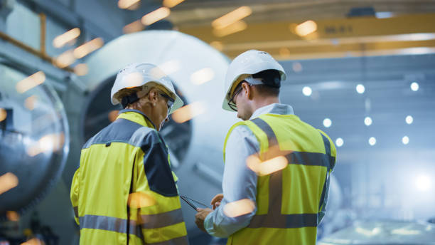 due ingegneri dell'industria pesante si trovano nella fabbrica di produzione di tubi, utilizzano tablet computer digitale, hanno una discussione. costruzione di un gasdotto per il trasporto di petrolio, gas e combustibili. scintille retro vista volare - plant facility foto e immagini stock