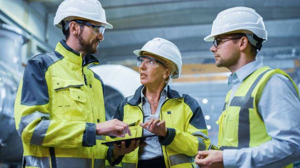 istock Three Heavy Industry Engineers Stand in Pipe Manufacturing Factory, Use Digital Tablet Computer, Have Discussion. Large Pipe Assembled. Design and Construction of Oil, Gas and Fuels Transport Pipeline 1224034127