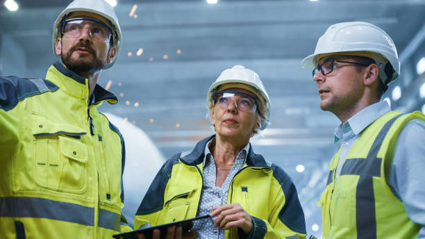 istock Three Heavy Industry Engineers Stand in Pipe Manufacturing Factory, Use Digital Tablet Computer, Have Discussion. Large Pipe Assembly. Design and Construction of Oil, Gas and Fuels Transport Pipeline 1224034134