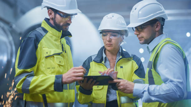 istock Three Heavy Industry Engineers Stand in Pipe Manufacturing Factory, Use Digital Tablet Computer, Have Discussion. Large Pipe Assembled. Design and Construction of Oil, Gas and Fuels Transport Pipeline 1224034144