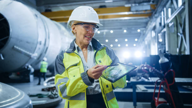istock Professional Heavy Industry Female Engineer Wearing Safety Uniform, Holds Digital Tablet Computer and Explains Product Design. Industrial Factory Construction of Oil, Gas and Fuels Transport Pipeline 1224034145