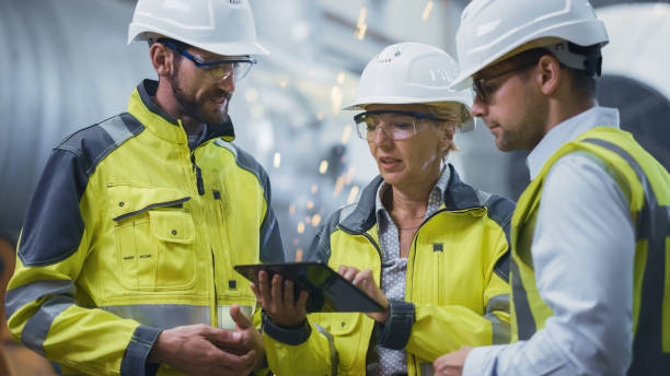 three heavy industry engineers stand in pipe manufacturing factory, use digital tablet computer, have discussion. large pipe assembled. design and construction of oil, gas and fuels transport pipeline - plant oil imagens e fotografias de stock