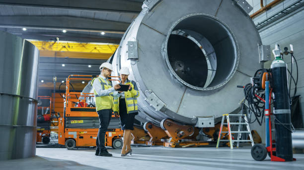 istock Two Heavy Industry Engineers Stand in Pipe Manufacturing Factory, Use Digital Tablet Computer, Have Discussion. Facility for Construction of Oil, Gas and Fuel Pipeline Transportation Products 1224034670