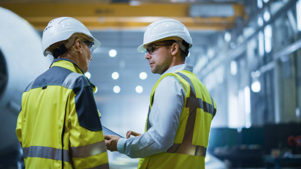 istock Two Heavy Industry Engineers Stand in Pipe Manufacturing Factory, Use Digital Tablet Computer, Have Discussion. Construction of Oil, Gas and Fuels Transport Pipeline. Back View Sparks Flying 1224034677