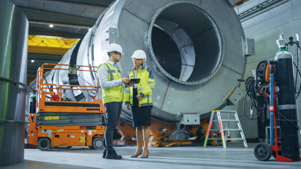 istock Two Heavy Industry Engineers Stand in Pipe Manufacturing Factory, Use Digital Tablet Computer, Have Discussion. Facility for Construction of Oil, Gas and Fuel Pipeline Transportation Products 1224034678