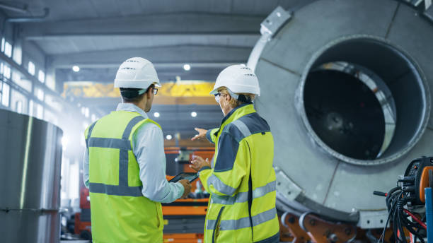 istock Two Heavy Industry Engineers Stand in Pipe Manufacturing Factory, Use Digital Tablet Computer, Have Discussion. Facility for Construction of Oil, Gas and Fuel Pipeline Transportation Products 1224034686