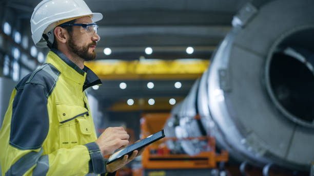 istock Heavy Industry Engineer in Pipe Manufacturing Factory, Use Digital Tablet Computer. Facility for Construction of Oil, Gas and Fuel Pipeline Transportation Products. Side View 1224034702