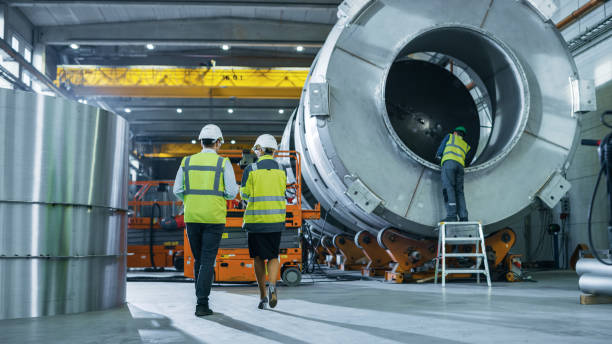 istock Two Heavy Industry Engineers Walk Through Pipe Manufacturing Factory, Use Digital Tablet Computer, Have Discussion. Facility for Construction of Oil, Gas and Fuel Pipeline Transportation Products 1224034710