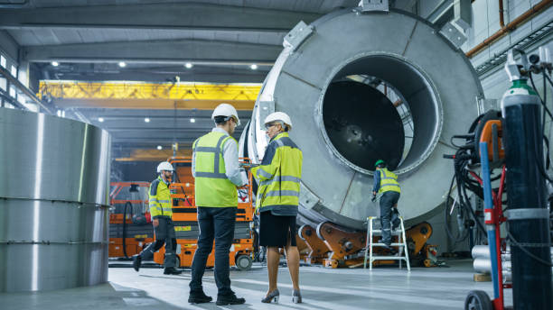 istock Two Heavy Industry Engineers Stand in Pipe Manufacturing Factory, Use Digital Tablet Computer, Have Discussion. Facility for Construction of Oil, Gas and Fuel Pipeline Transportation Products 1224034718