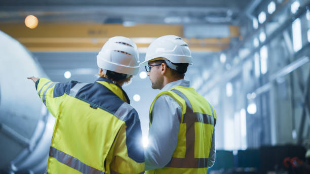 istock Two Heavy Industry Engineers Stand in Pipe Manufacturing Factory, Use Digital Tablet Computer, Have Discussion. Construction of Oil, Gas and Fuels Transport Pipeline. Back View Sparks Flying 1224034724