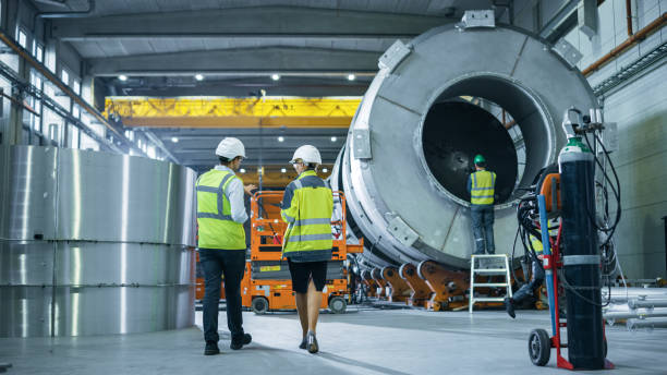 istock Two Heavy Industry Engineers Walk Through Pipe Manufacturing Factory, Use Digital Tablet Computer, Have Discussion. Facility for Construction of Oil, Gas and Fuel Pipeline Transportation Products 1224034737