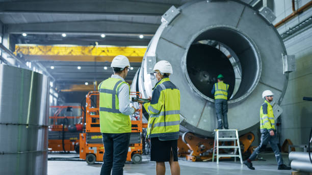 istock Two Heavy Industry Engineers Walk Through Pipe Manufacturing Factory, Use Digital Tablet Computer, Have Discussion. Facility for Construction of Oil, Gas and Fuel Pipeline Transportation Products 1224034738
