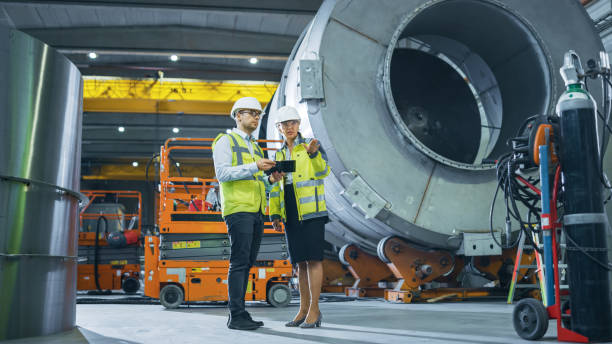 istock Two Heavy Industry Engineers Stand in Pipe Manufacturing Factory, Use Digital Tablet Computer, Have Discussion. Facility for Construction of Oil, Gas and Fuel Pipeline Transportation Products 1224034757