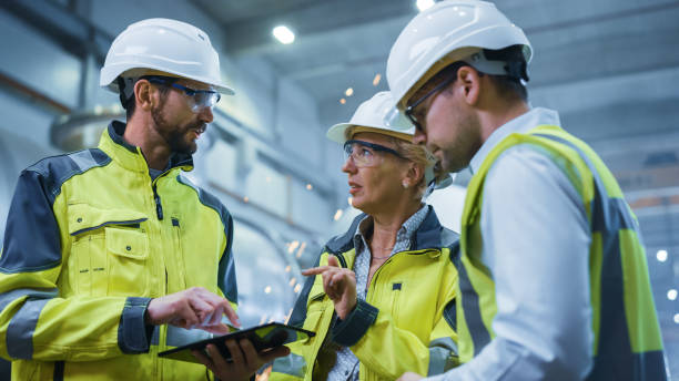 istock Three Heavy Industry Engineers Stand in Pipe Manufacturing Factory, Use Digital Tablet Computer, Have Discussion. Large Pipe Assembled. Design and Construction of Oil, Gas and Fuels Transport Pipeline 1224034763
