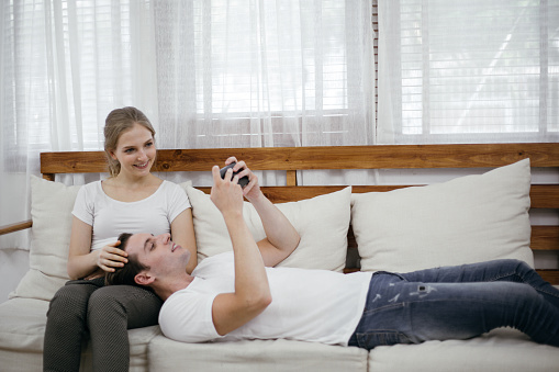 Happy cheerful romantic couple lying on couch playing chatting social media on smartphone in living room. stay at home self-quarantine preventing Coronavirus crisis. family lifestyle insurance