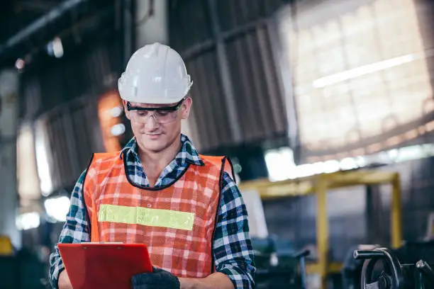 Photo of Portrait handsome smart engineer male manager working on construction repair checklist document in modern industrial manufacturing factory. worker man in protective uniform work hard. copy space