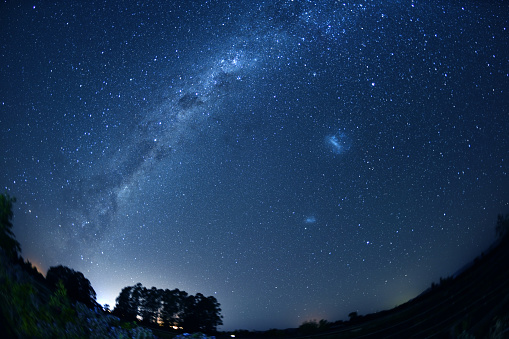 Bright Milky Way and Magellanic Clouds visible in January near Kaikoura City (lights on the horizon), Southern Island, New Zealand. Southern Cross constellation in the upper-left part of the picture.