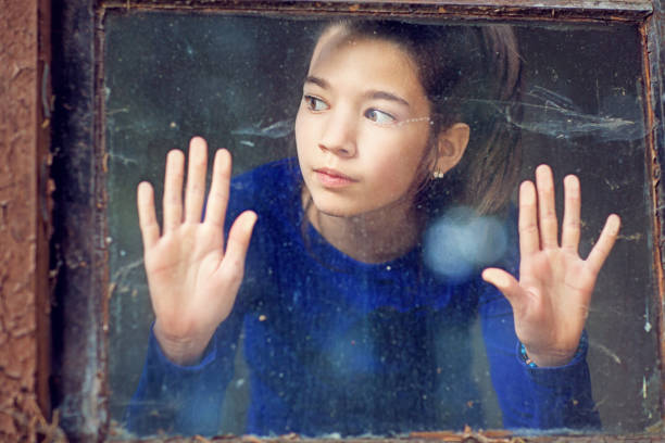 istock Sad young girl is standing at the window 1224039944