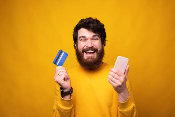 istock Smiling bearded hipster is holding a phone and a credit or debit card. 1224040105