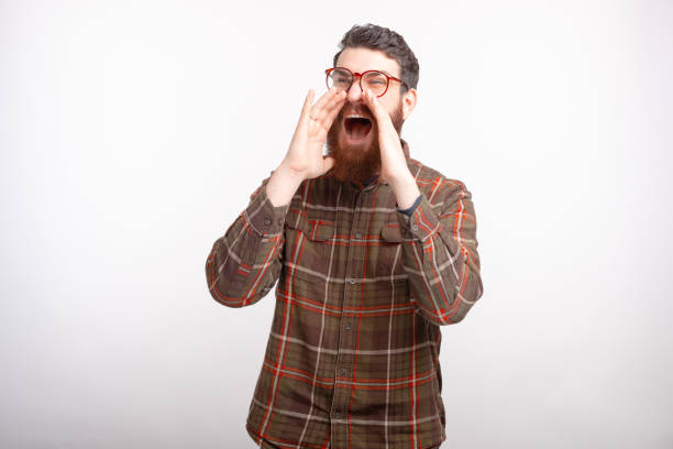 istock Young bearded man is shouting with hands over the month on white background. 1224040123