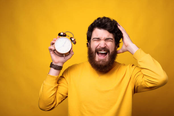 istock Bearded guy is screaming with hand on head while holding an alarm clock. 1224040751