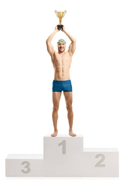 male swimmer lifting a gold trophy cup on a winners podium - swimming male isolated swimming goggles imagens e fotografias de stock