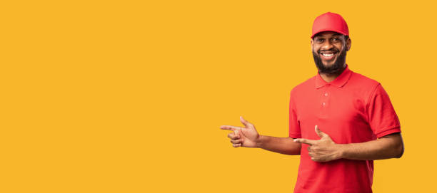istock Delivery Worker Pointing Fingers Aside At Copyspace, Studio Shot, Panorama 1224041068
