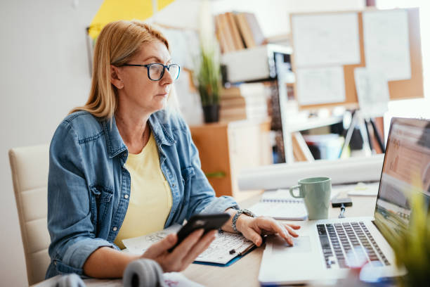 istock Mature woman working from home on laptop and using mobile app 1224041716