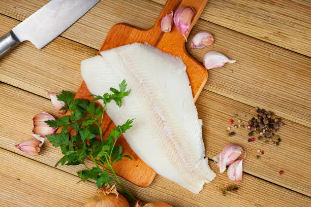 Fresh raw halibut fillet with greens and spices on wooden background. Cooking ingredients